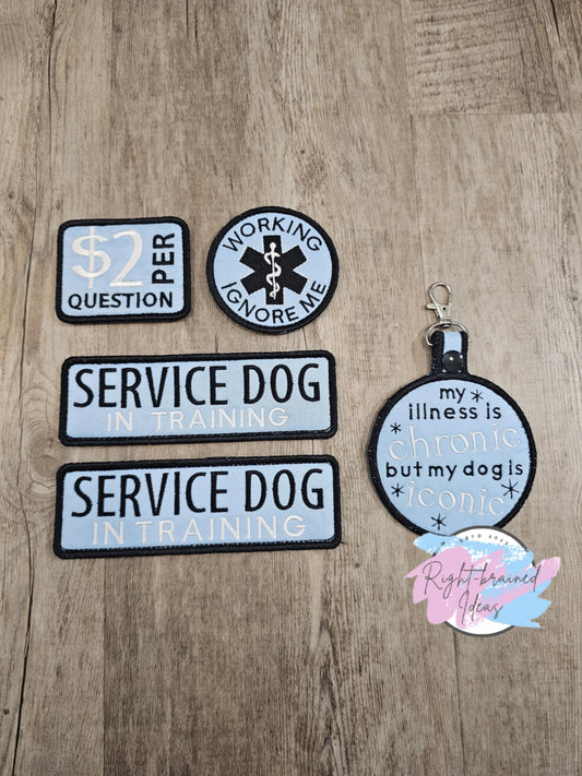 This is a basic four-piece set made with light blue twill and black and white embroidery. Patches have velcro sewn on back. The patch tab has a black plastic snap enclosure with metal d-ring clasp.&nbsp;
Set includes:&nbsp;
(2) 2in x 6in rectangular patches: "Service Dog, In Training"
(1) 3in x 2.5in rectangular patch: "$2 Per Question"&nbsp;
(1) 3.5in x 6in circular patch tab: "My illness is chronic, but my dog is iconic" with star symbols surrounding the text.

(1) 3in circular patch: "Working, Ignore Me"