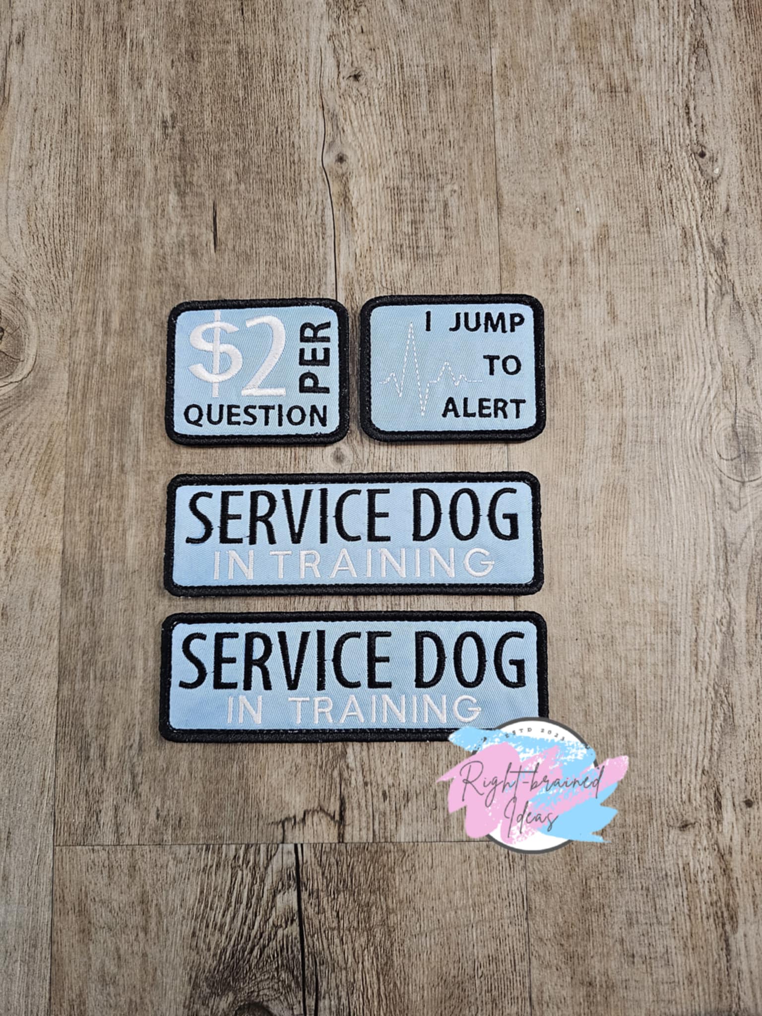 This is a basic four-piece patch set made with blue twill and black and white embroidery thread. All patches have velcro sewn on the back.&nbsp;

Set Includes:&nbsp;

(2) 6in x 2in rectangular patches: "Service Dog In Training"

(2) 2.5in x 3in rectangular patches: "$2 Per Question" and "I Jump To Alert" next to an EKG symbol