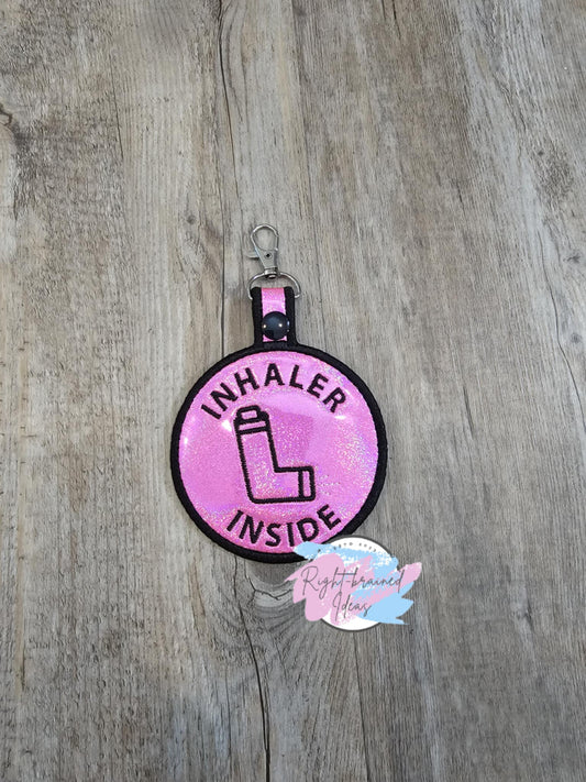 Inhaler Inside Black on Sparkle Pink Holographic Patch Tab

It has a black plastic snap enclosing a metal d-ring clip.&nbsp;

Includes:
(1) 3.5in x 6in circular patch tab: "Inhaler Inside" around a inhaler symbol