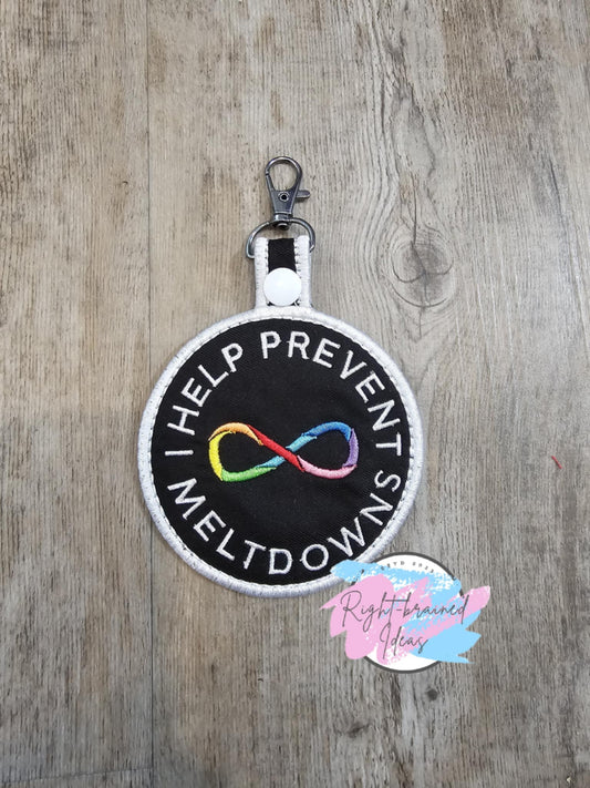 This is a Neurodivergent Inspired patch tab made of black twill with rainbow and white embroidery thread. It has a white plastic snap enclosing a metal d-ring clip.

(1) 3.5in x 6in circular patch tab: "Help Prevent Meltdowns" around a Rainbow Mobius/Infinity Loop in the center of the patch tab.
